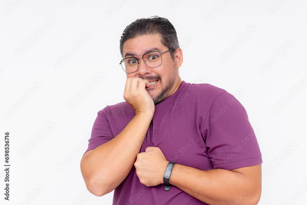 A middle aged bespectacled man biting his fingers in fear. Wearing a purple waffle shirt, isolated on a white background. A middle aged bespectacled man biting his fingers in fear. Wearing a purple waffle shirt, isolated on a white background.