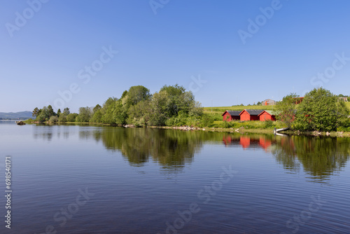 Serene lake Snasavatnet in Steinkjer, Norway, with the wooden Kvam Church peeking through tree branches along the shore