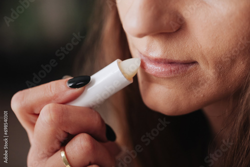 Woman using petrolatum on her mouth. Closeup lips background. Applying lip salve on lips with lipstick. Beauty background. Young girl skin care. Cosmetics for moisturize. Happy woman smile. photo