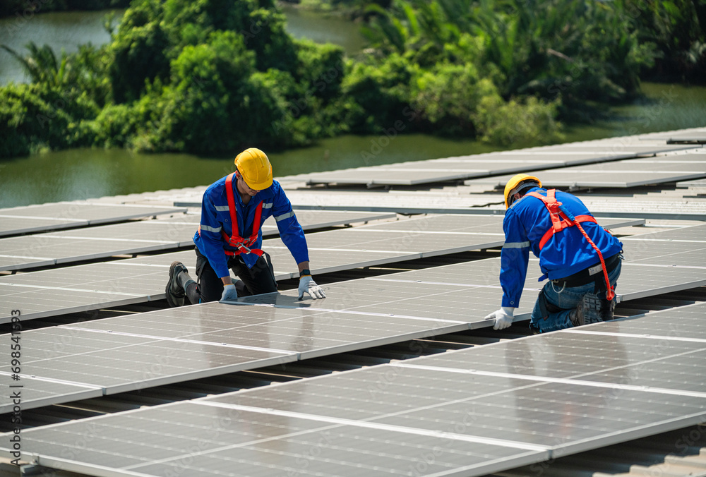 Men technicians carrying photovoltaic solar modules on the factory roof. Engineers in helmets installing solar panel systems outdoors. Concept of alternative and renewable energy.
