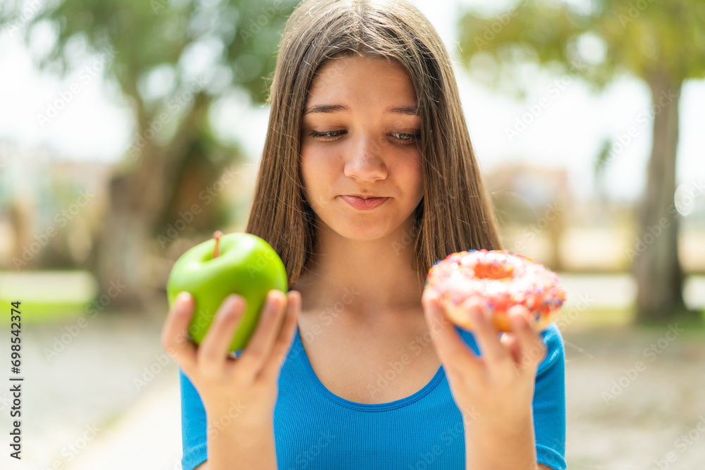 Teenager girl at outdoors holding apple and donut Teenager girl at outdoors holding apple and donut