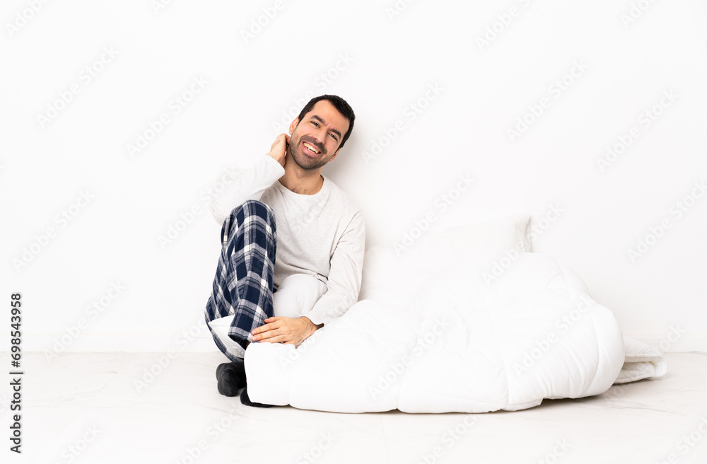 Caucasian man in pajamas sitting on the floor at indoors laughing