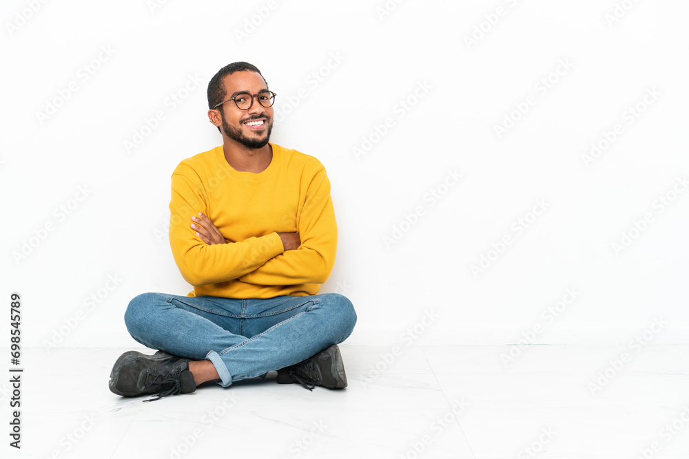 Young Ecuadorian man sitting on the floor isolated on white wall with arms crossed and looking forward Young Ecuadorian man sitting on the floor isolated on white wall with arms crossed and looking forward