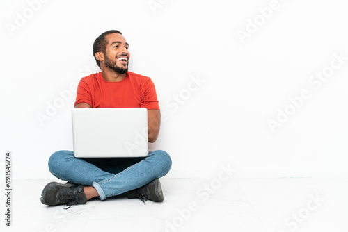 Young Ecuadorian man with a laptop sitting on the floor isolated on white background happy and smiling photo