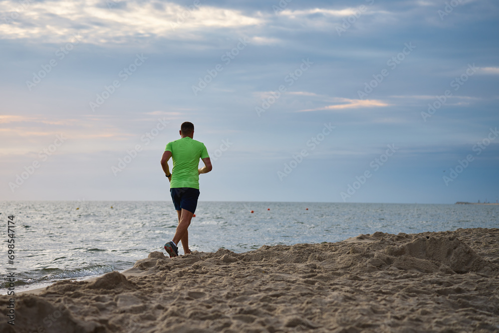 Back view of man jogging along sea beach at morning, Male athlete running along the shoreline