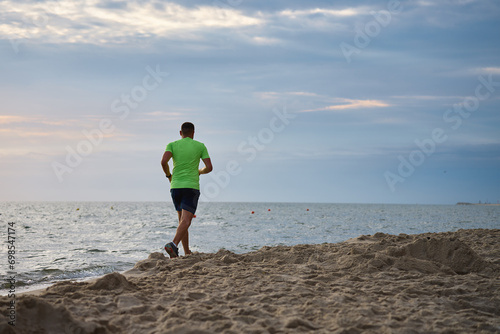 Back view of man jogging along sea beach at morning, Male athlete running along the shoreline © Lazy_Bear