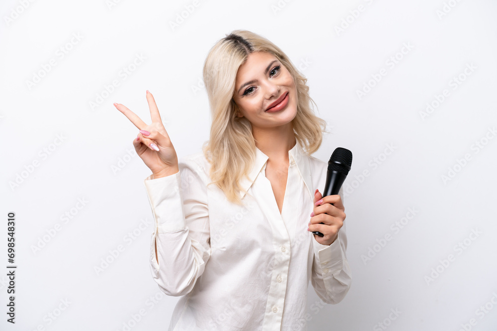 Young singer woman picking up a microphone isolated on white background smiling and showing victory sign Young singer woman picking up a microphone isolated on white background smiling and showing victory sign