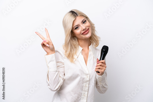Young singer woman picking up a microphone isolated on white background smiling and showing victory sign