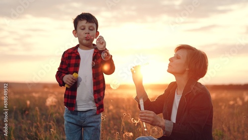 Boy with mother comes to make bubbles source of entertainment at sunset. Boy with mother adorning activity. Boy with mother spends time with positive emotions blowing bubbles on field at back sunset