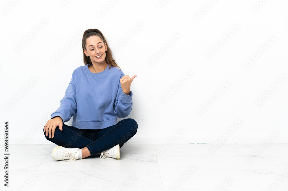 Young woman sitting on the floor pointing to the side to present a product Young woman sitting on the floor pointing to the side to present a product