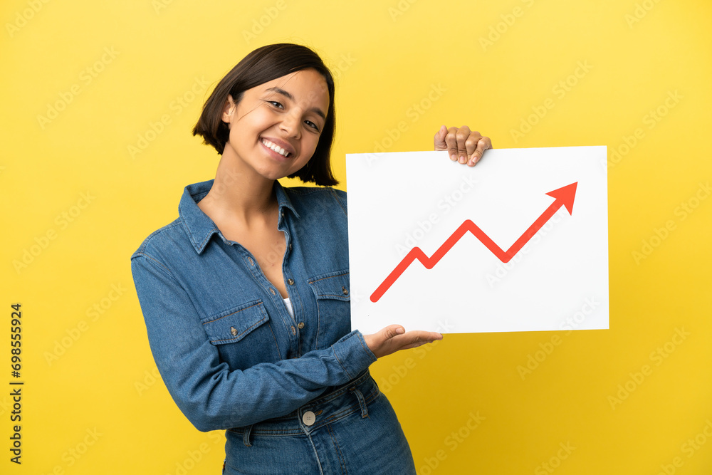 Young mixed race woman isolated on yellow background holding a sign with a growing statistics arrow symbol Young mixed race woman isolated on yellow background holding a sign with a growing statistics arrow symbol