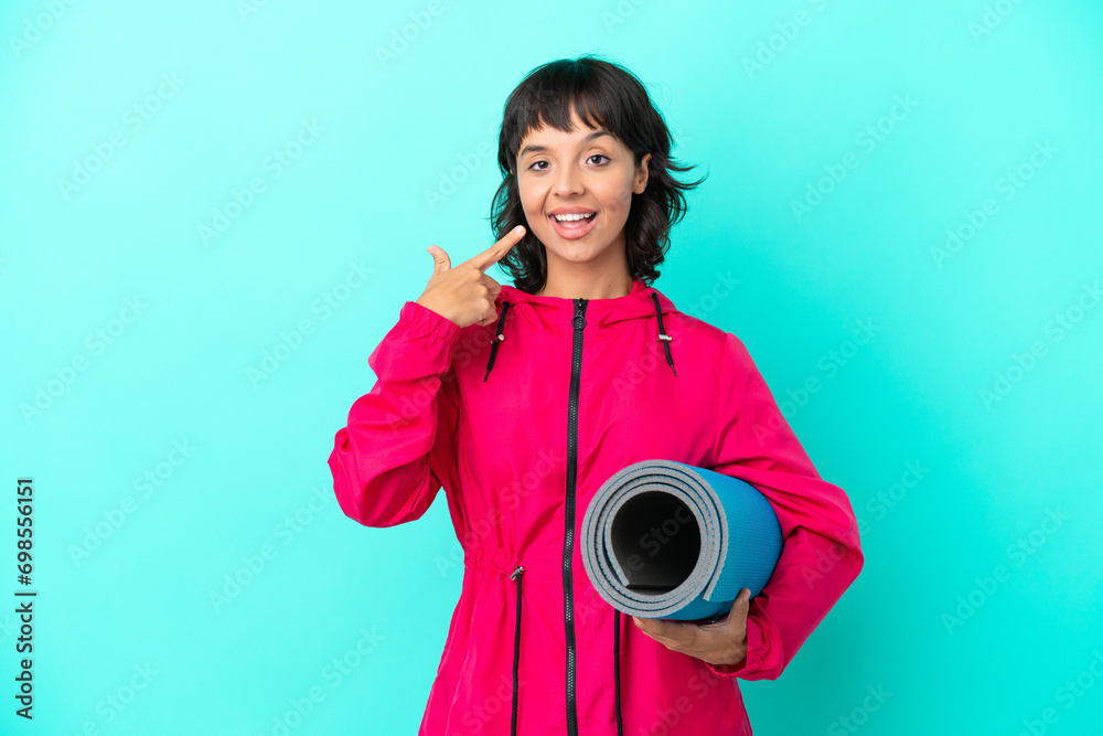 Obraz premium Young girl going to yoga classes while holding a mat isolated on blue background giving a thumbs up gesture
