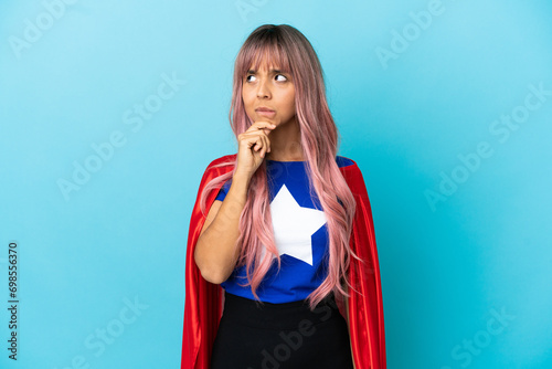 Young superhero woman with pink hair isolated on blue background having doubts and thinking