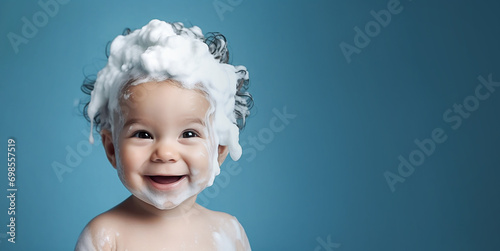 Little smiling baby boy with big soap foam on her head in her hair on a blue background. Copy space photo