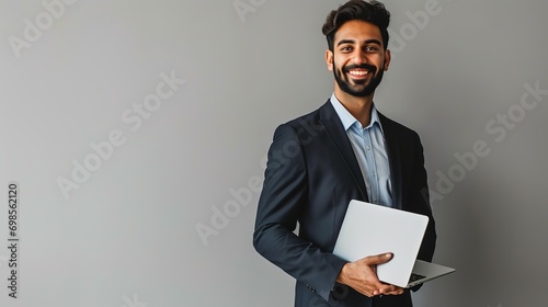 Happy smiling business man employee or manager standing isolated on gray background holding laptop advertising online products, business trainings and webinars photo