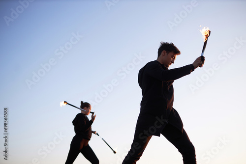 Side view at two fire show performers dancing with flames outdoors against clear sky, copy space photo