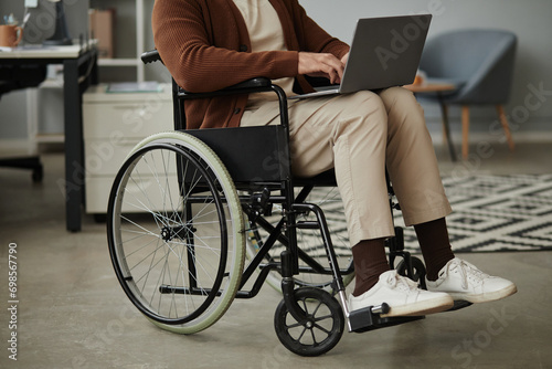 Close up of unrecognizable man with disability using laptop sitting in wheelchair at office, copy space photo