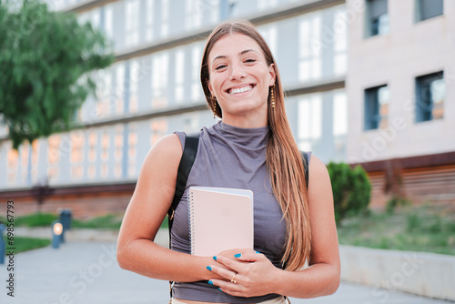 Portrait of a joyful and adorable teenage blonde woman posing for a college promotion holding a notebook. Happy caucasian young student female looking at camera enjoying with a perfect white teeth