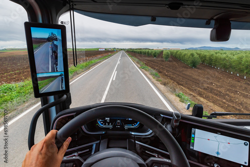 View from the driver's position of a truck of a road in the middle of crop fields and the driver guided by the GPS on the dashboard screen, rearview mirror with camera and screen.