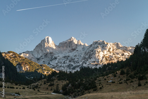 Gorgeous winter mountain panorama showcasing snow-capped peaks, serene valleys, and icy streams against a crisp blue sky backdrop.