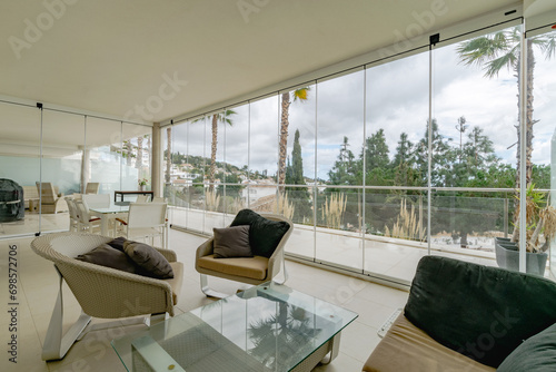 a Mediterranean apartment terrace surrounded by glass windows and filled with chairs.