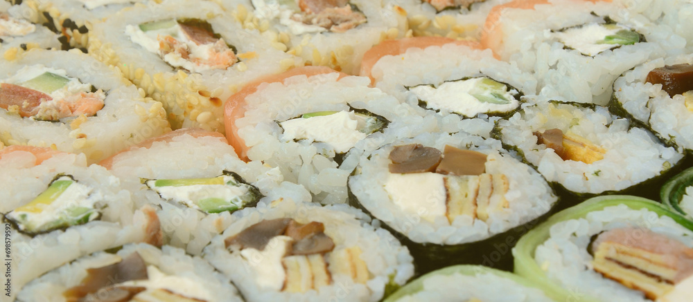 Close-up of a lot of sushi rolls with different fillings lie on a wooden surface. Macro shot of cooked classic Japanese food with a copy space. Close-up of a lot of sushi rolls with different fillings lie on a wooden surface. Macro shot of cooked classic Japanese food with a copy space.