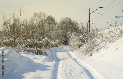 The road that lies parallel to the railway line is covered with snow on a sunny day after a heavy snowfall