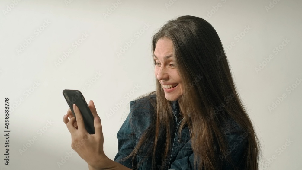 Portrait of appealing female model in friendly mood. Brunette woman in casual on white background in the studio looks at smartphone and smiles. Portrait of appealing female model in friendly mood. Brunette woman in casual on white background in the studio looks at smartphone and smiles.