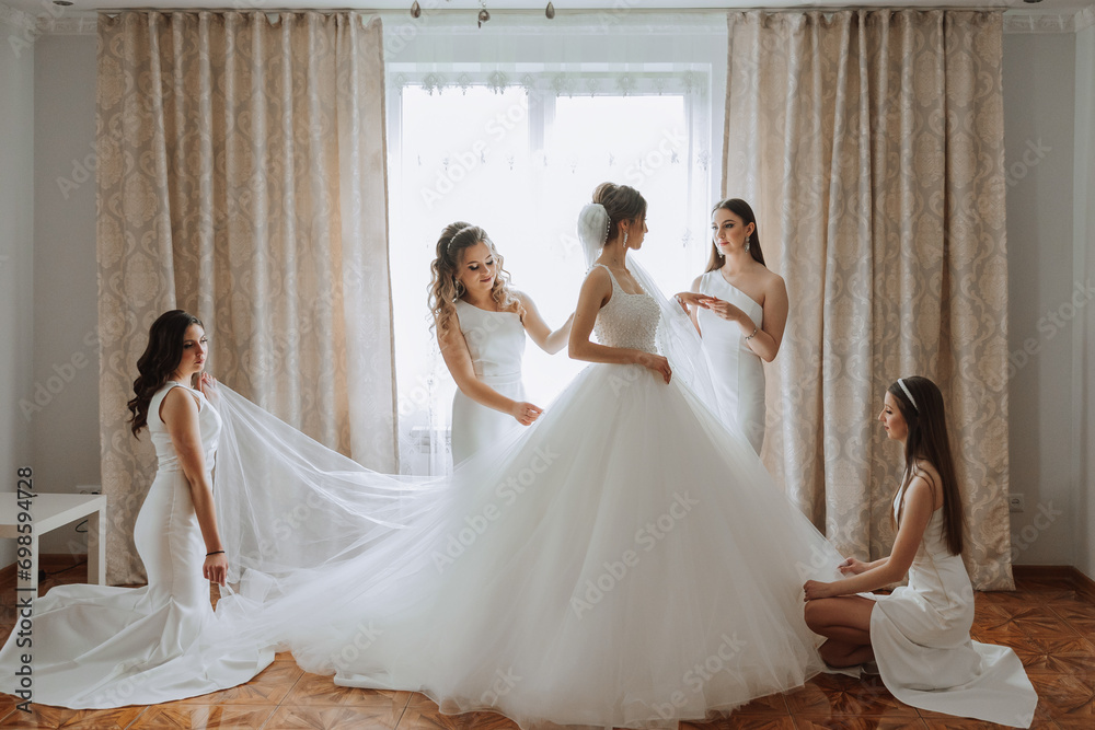 Fototapeta premium Friends rejoice with the bride in the morning. They take pictures, smile, help the bride fasten her dress.