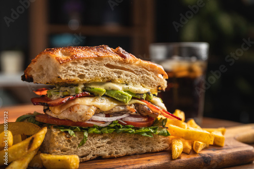 Grilled chicken breast sandwich with lettuce, tomato, bacon, red onion rings and avocado served on artisan bread and a portion of French fries photo