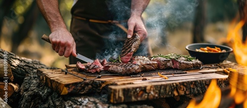 Man grills steak on wooden board outdoors for a summer picnic.