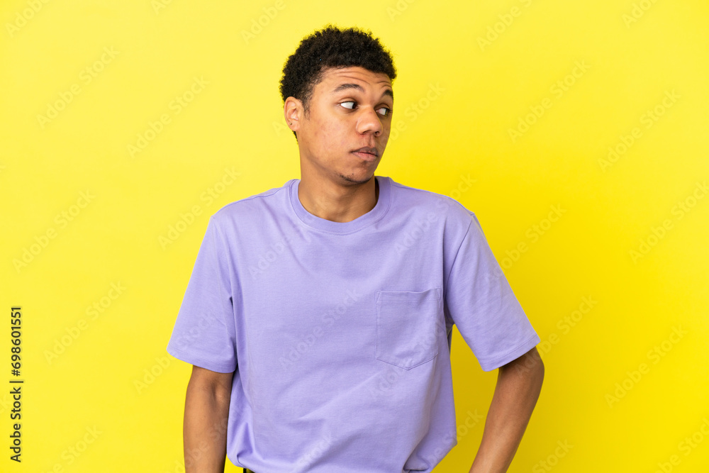Young African American man isolated on yellow background making doubts gesture looking side Young African American man isolated on yellow background making doubts gesture looking side