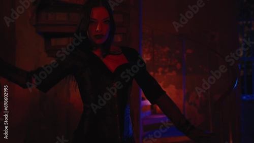 A gorgeous girl in a total black Halloween costume playing with fireworks near the stairs with candles. Sparkle in her hand. Nighttime, outdoor, slow motion. 