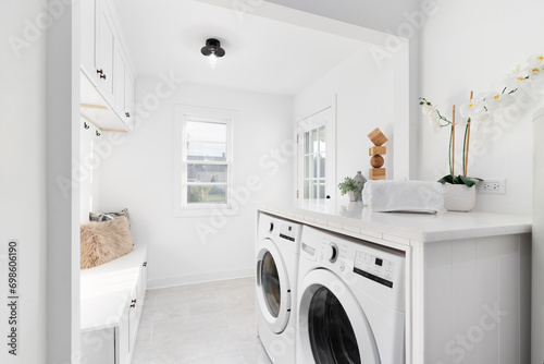 A remodeled laundry room and mud room with new appliances, tiled floor, and bench with cabinets above. No brands or logos.