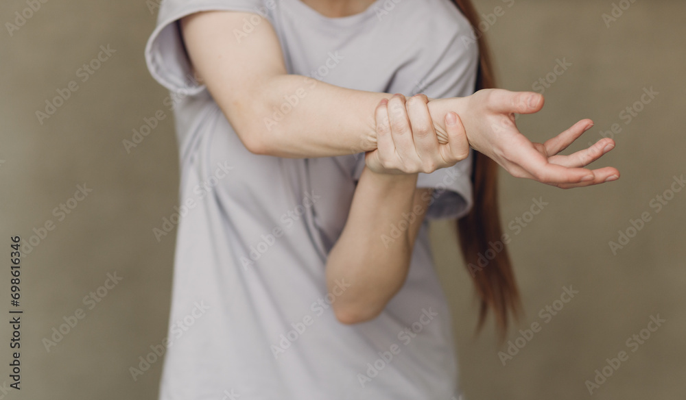 Young woman with hand convulsions pain ache against brown background Young woman with hand convulsions pain ache against brown background