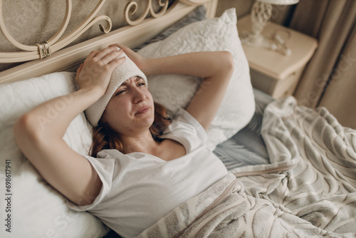 Young woman with headache flu ill sick disease cold at home indoor lying on bed with cold compress on her head at bedroom home photo