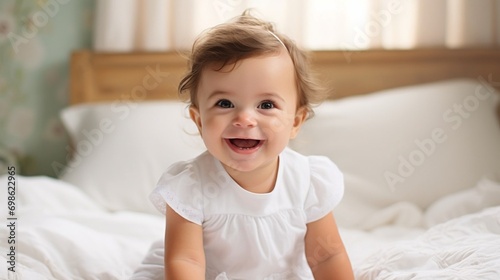 portrait of a little cute smiling baby in white clothes lying on bed in bedroom.