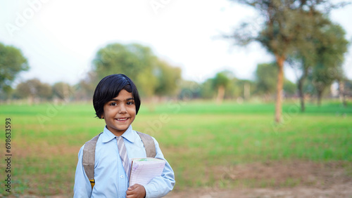 Smiling student girl wearing school backpack and holding exercise book. Portrait of happy asian village girl at green farmland. Face of smiling school girl looking at camera.