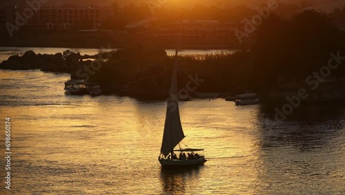 Aswan, Egypt - November 29 2023: Traditional felucca boats sail along the Nile river during a dramatic sunset in Egypt. Shot from the Feryal garden. 