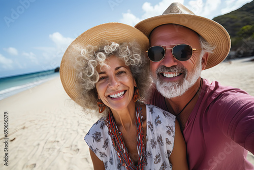 Pareja de mujer y hombre felices y enamorados  de 60 años, haciendose un selfie en una playa paradisiaca, con gorros de paja. Concepto celebraciones, vacaciones, aniversarios, San Valentin photo