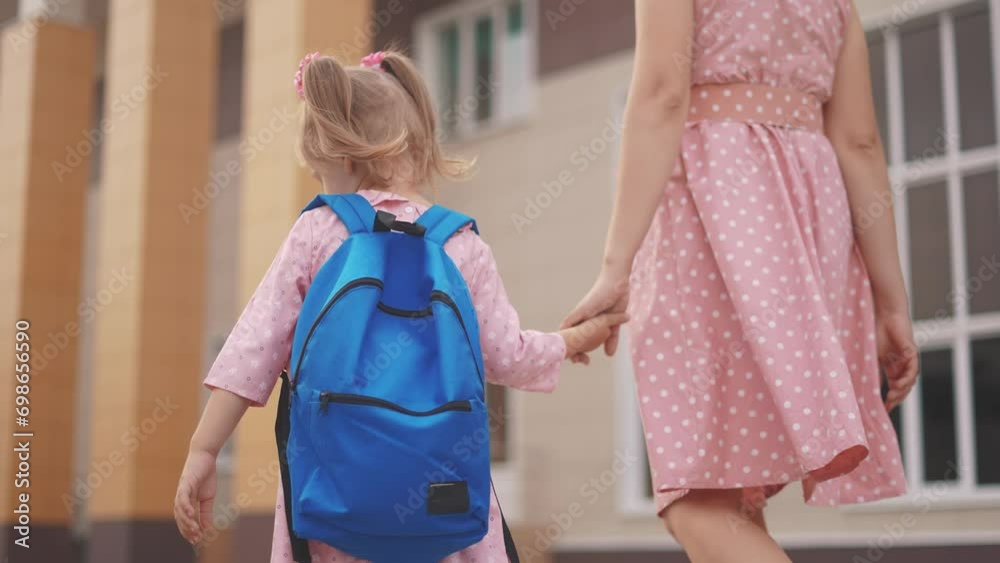 back to school. a mother and daughter go to school holding hands view ...