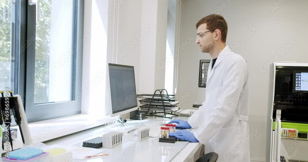 Man laboratory technician in medical coat and glasses working in hospital with modern equipment. Male doctor specialist examining blood samples and using computer in clinic lab Man laboratory technician in medical coat and glasses working in hospital with modern equipment. Male doctor specialist examining blood samples and using computer in clinic lab