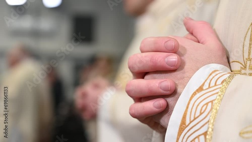 Catholic priests in liturgical vestments praying with hands folded. Hands of Christian man praying in Cathedral. Christmas Midnight Mass in church.   photo