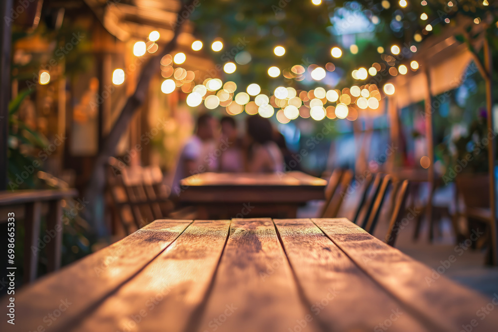 A romantic outdoor dining setting with a wooden table under a canopy of twinkling lights and a blurred couple in the background - obrazy, fototapety, plakaty 