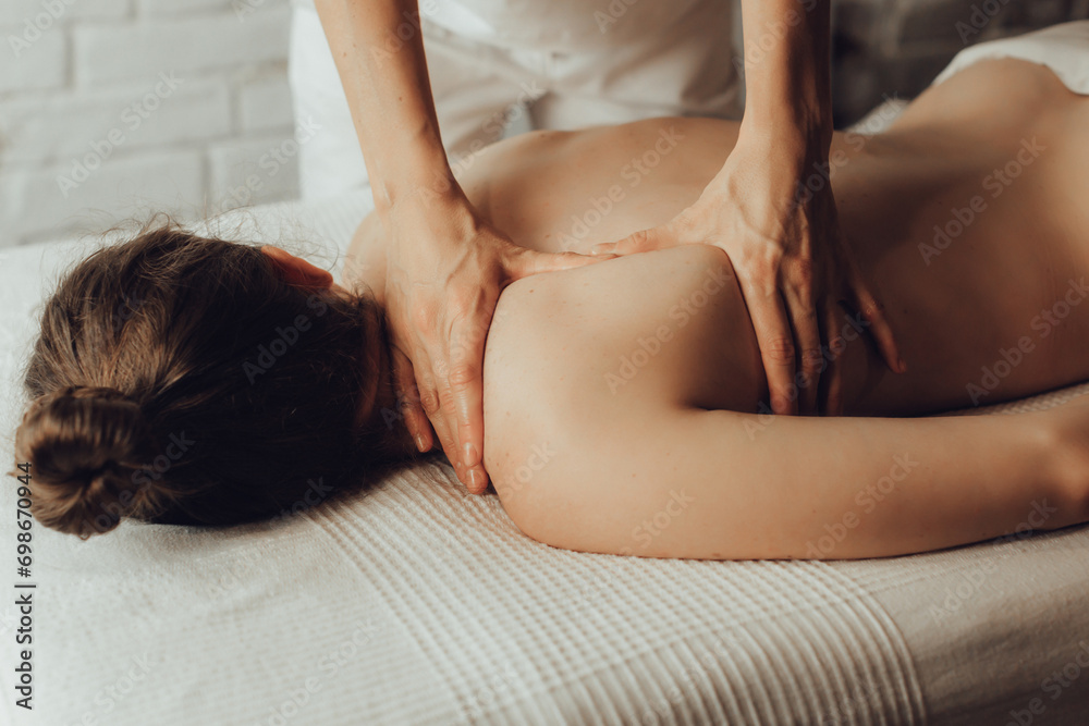 Obraz premium Hands of female chiropractor massaging shoulders of young woman lying on massage table. Concept of physical therapy treatment ,neck pressure point