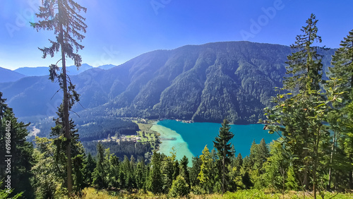 Aerial view of east bank of alpine lake Weissensee in Carinthia, Austria. Pristine turquoise water of bathing lake. Tranquil forest in serene landscape in remote untouched nature in summer. Vacation © Chris