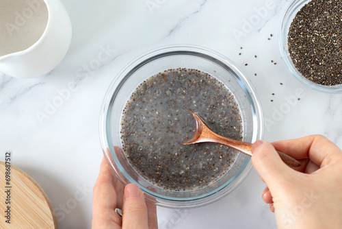 Hands holding and preparing a bowl chia seed pudding with plant-based milk in the kitchen. Top table view. Preparation of healthy breakfast food concept.