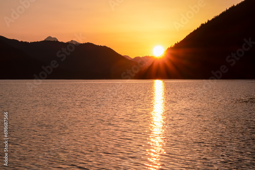 Breathtaking allure of sunset at alpine lake Weissensee in remote Austrian Alps in Carinthia. Embrace serene ambiance as tranquil surface of water amplifies sun gentle rays. Sun gracefully descends photo