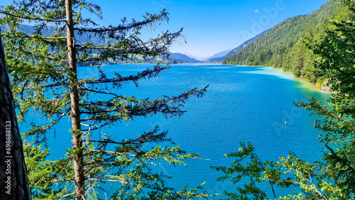 Panoramic view of alpine landscape seen from east bank of lake Weissensee in Carinthia, Austria. Tranquil forest in serene landscape amidst remote untouched nature in summer. Pristine turquoise water photo