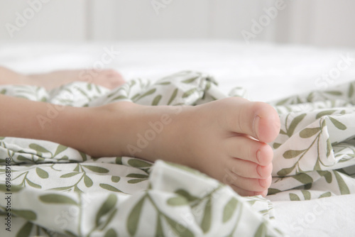 Child feet under cotton bedcover under soft morning light 